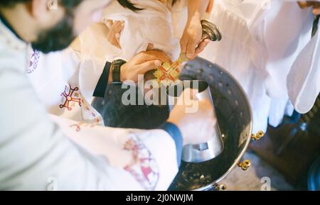 Priest washes the baby head from a jug during baptism over a basin Stock Photo