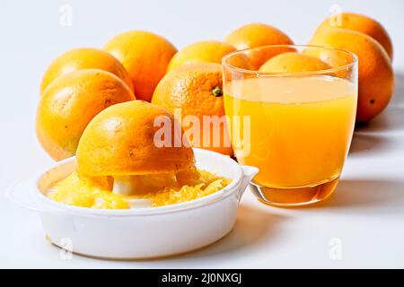Orange juicer with freshly squeezed orange with glass of orange juice and whole oranges in background Stock Photo