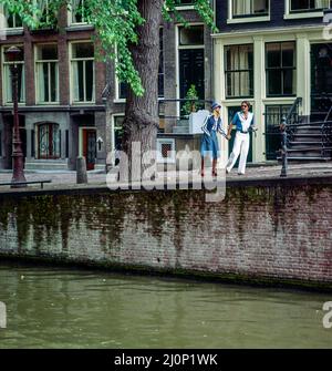 Vintage Amsterdam 1970s, stylish young couple strolling beside canal, houses, Holland, Netherlands, Europe, Stock Photo