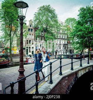 Vintage Amsterdam 1970s, stylish young couple strolling on canal's bridge, houses, Holland, Netherlands, Europe, Stock Photo