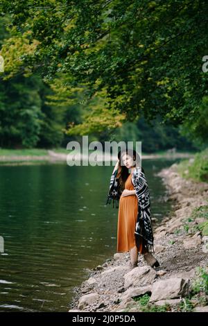 Pregnant woman stands on the shore of a lake in a green forest Stock Photo