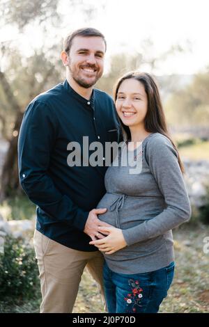 Smiling man holding hands on belly of pregnant woman Stock Photo