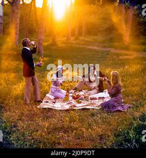 Vintage Italy 1970s, 2 couples of cheerful friends having a picnic at sunset, solar light flare, late afternoon, Roman countryside, Lazio, Europe, Stock Photo