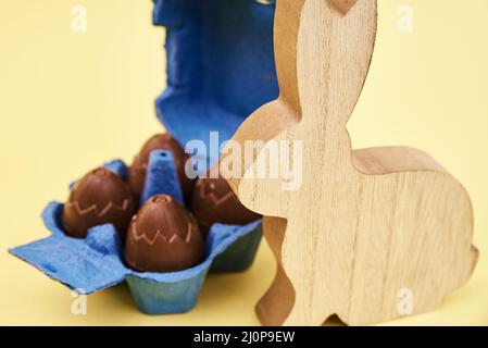 Wooden rabbit and chocolate eggs on yellow background, Happy Easter card Stock Photo