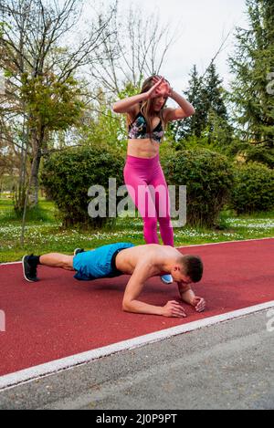 Portrait of a young handsome couple doing pushups exercises at the park. healthy concept. Outdoors. Stock Photo