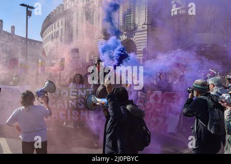 London, UK. 19th Mar, 2022. A protester holds a smoke flare while chanting slogans through a megaphone during the demonstration in Piccadilly Circus. Demonstrators marched through Central London in protest against racism and in support of refugees. Credit: SOPA Images Limited/Alamy Live News Stock Photo