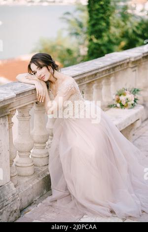 Bride sits on a stone bench with her head resting on a stone balustrade Stock Photo
