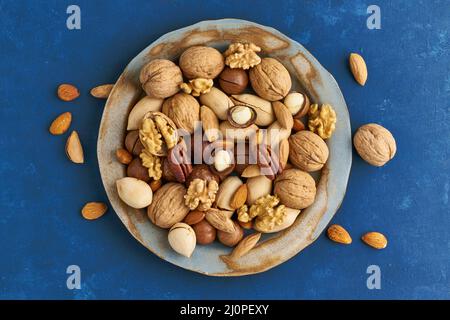 Classic blue in food. Mix of nuts on plate - walnut, almonds, pecans, macadamia and knife for opening shell. Healthy vegan food. Stock Photo