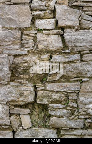 A grey old stone wall with moss between the stones. Beige stone background. Stock Photo