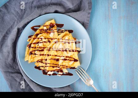 Two pancakes with chocolate syrup, almond flakes on plate, honey flows from spoon Stock Photo