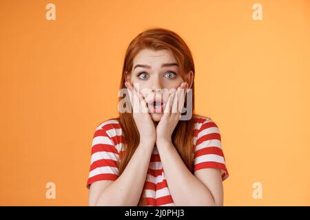 Close-up shocked speechless redhead woman, drop jaw gasping, touch cheeks embarrassed shook, look pity shame, stare camera aston Stock Photo