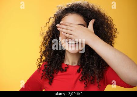 Close-up shot of dreamy happy young cute woman with curly hair covering eyes with palm as counting or playing peekaboo smiling b Stock Photo