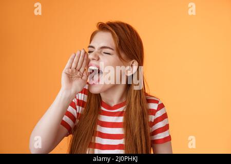 Hey where are you. Cute carefree redhead funny girl hold hand near opened mouth turn left close eyes, yelling out loud, searchin Stock Photo