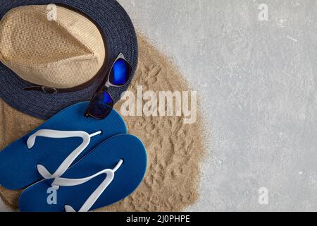 Straw hat, flip flops and sunglass on scattered sea sand against a light gray concrete background. Summer beach holiday concept. Top view with copy sp Stock Photo