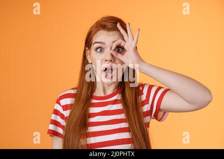 Surprised excited shocked young redhead girl gasping impressed look through okay circle, stare camera astonished awesome sale, o Stock Photo