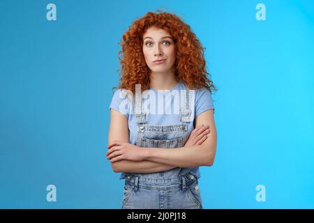 Unsure confused redhead curly woman look perplexed uncertain cross arms chest smirking stare camera full disbelief suspicious do Stock Photo