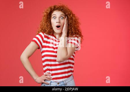 Shocked amused emotive redhead ginger girl curly haircut popping eyes stare camera fascinated impressed open mouth gasping enter Stock Photo