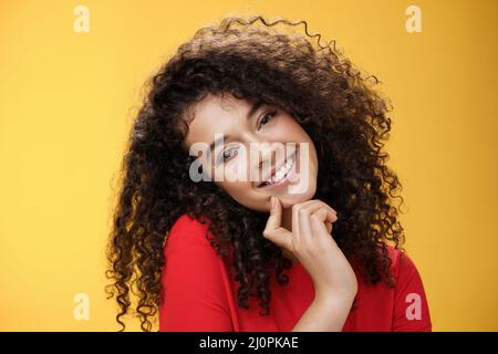 Close-up shot of charming flirty and silly curly-haired young woman making faces as trying get what wants, smiling tilting head Stock Photo