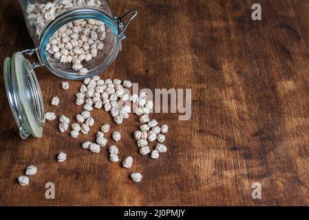 Pot lying with chickpeas scattered on a wooden table. Stock Photo
