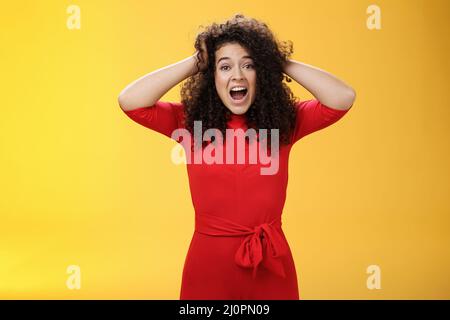 Girl feeling pressure standing anxious in panic holding hands on curly hair yelling at camera disturbed, freaked out being tense Stock Photo