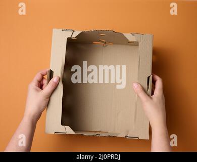 Female hands are holding an empty open box of brown cardboard, top view, concept of packing things Stock Photo