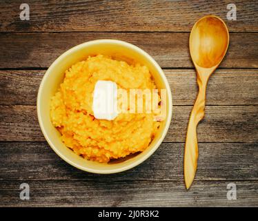 Bowl with pumpkin rice porridge with milk and a piece of butter and a wooden spoon on a wooden background top view close up Stock Photo