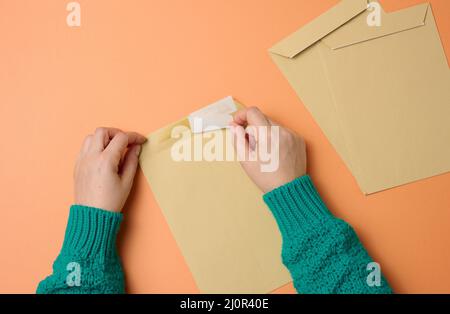 Female hand holds paper envelopes on an orange background, top view. Correspondence Stock Photo