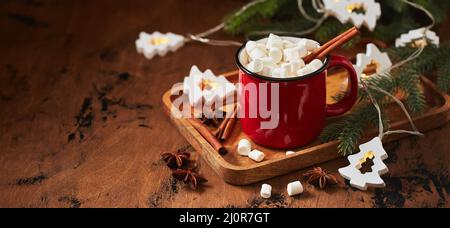 Red cup of hot cocoa with marshmallows on wooden table with christmas tree for christmas Stock Photo