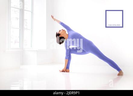 Young slender fit woman in very peri long bodysuit performing yoga pose, isolated over white studio background Stock Photo