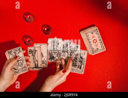 Tarot cards and female hands of fortune teller on red background Stock Photo