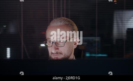 Middle-aged male office employee working late in dark office. Modern office worker working overtime Stock Photo