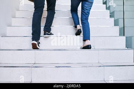 Reaching their goals together. Rearview shot of two unrecognisable businesspeople walking up a staircase together in an office. Stock Photo