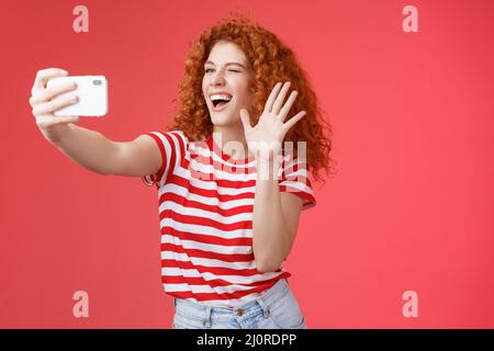 Cheerful friendly energized good-looking redhead curly-haired female send hello waving palm smiling broadly blogger record life Stock Photo