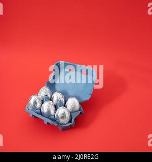Creative Easter concept of cardboard box of eggs painted in silver aluminum foil. Pastel red background. Stock Photo