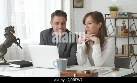 Happy business people working at desk using laptop computer, talking, working together Stock Photo