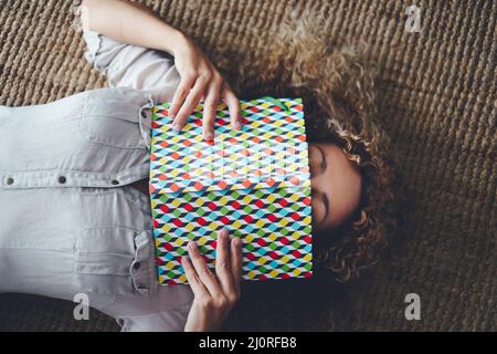 Adult lady asleeping on the carpet at home. People sleeping on the floor indoor with colorful book on the face. Tired female in vertical above view po Stock Photo