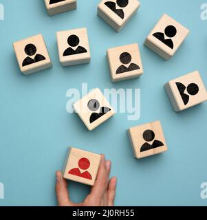 Female hand holds a wooden block on a blue background. Recruitment concept, teamwork, effective management Stock Photo