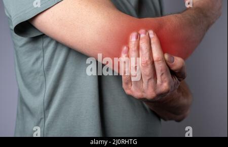 Man suffering from elbow pain and holding painful hand with red point closeup. Hand injury. Health care, joint diseases concept. High quality photo Stock Photo