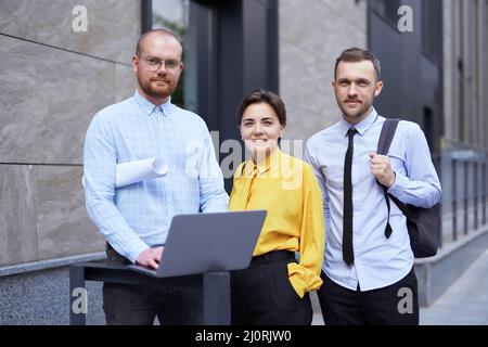 Business or finance industry theme. Team of successful managers working outdoor in city downtown and discussing project presentation, talking or brainstorming using laptop. High quality image Stock Photo