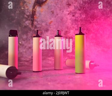 multicolored electronic cigarettes vape on pink background with smoke Stock Photo