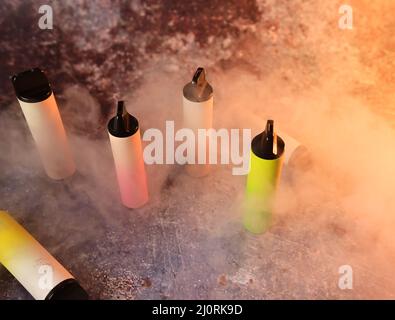 multicolored electronic cigarettes vape on dark background with smoke Stock Photo