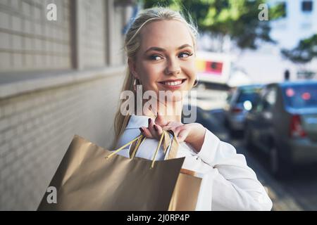 Retail therapy looks good on her. Cropped shot of an attractive young woman looking away thoughtfully while holding shopping bags in the city during Stock Photo