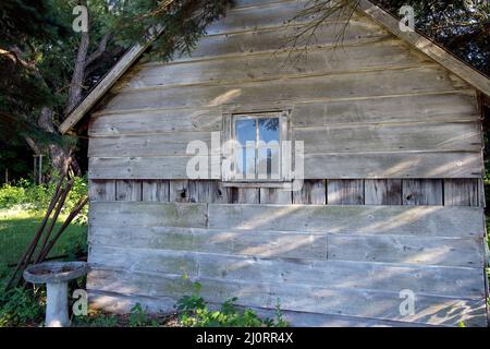 Rustic cabin with stone birdbath and square window in woods Stock Photo