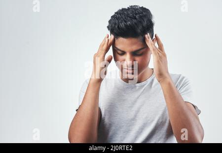 Ive been getting these headaches more often. Studio shot of a young man suffering from a headache while standing against a white background. Stock Photo