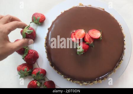 Chocolate cake with chocolate ganache and topped with walnut and fresh strawberries. Shot on white background. Stock Photo