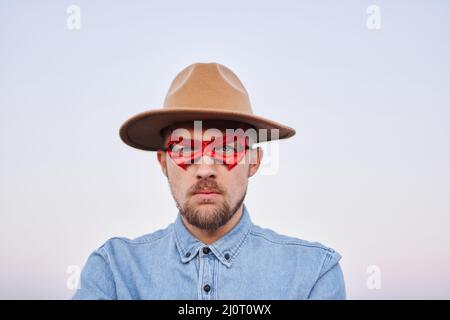 Cute bearded caucasian man in red superhero mask and jeans shirt posing with serious face in front of the camera. Strength, superpower or justice concept. High quality image Stock Photo