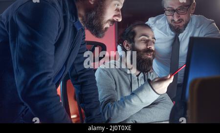 Three male colleague workers collaborating in office talking while looking at computer screen together at workplace Stock Photo