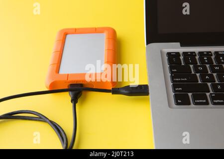 external hard drive on a yellow background connected to a laptop computer USB port Stock Photo