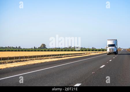 Classic long haul big rig white semi truck tractor with truck driver cab sleeping compartment transporting cargo in refrigerator semi trailer running Stock Photo