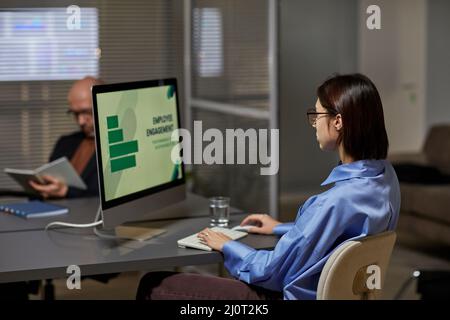 Back view at female marketing manager working in office at night while analyzing data on screen, copy space Stock Photo